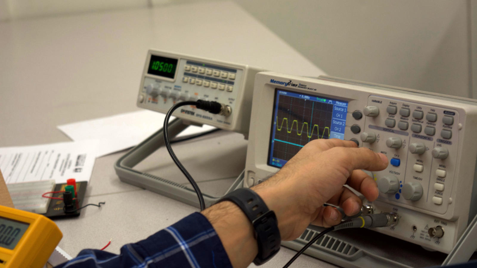 An electronics student adjusts an oscilloscope to measure voltage change in a circuit.