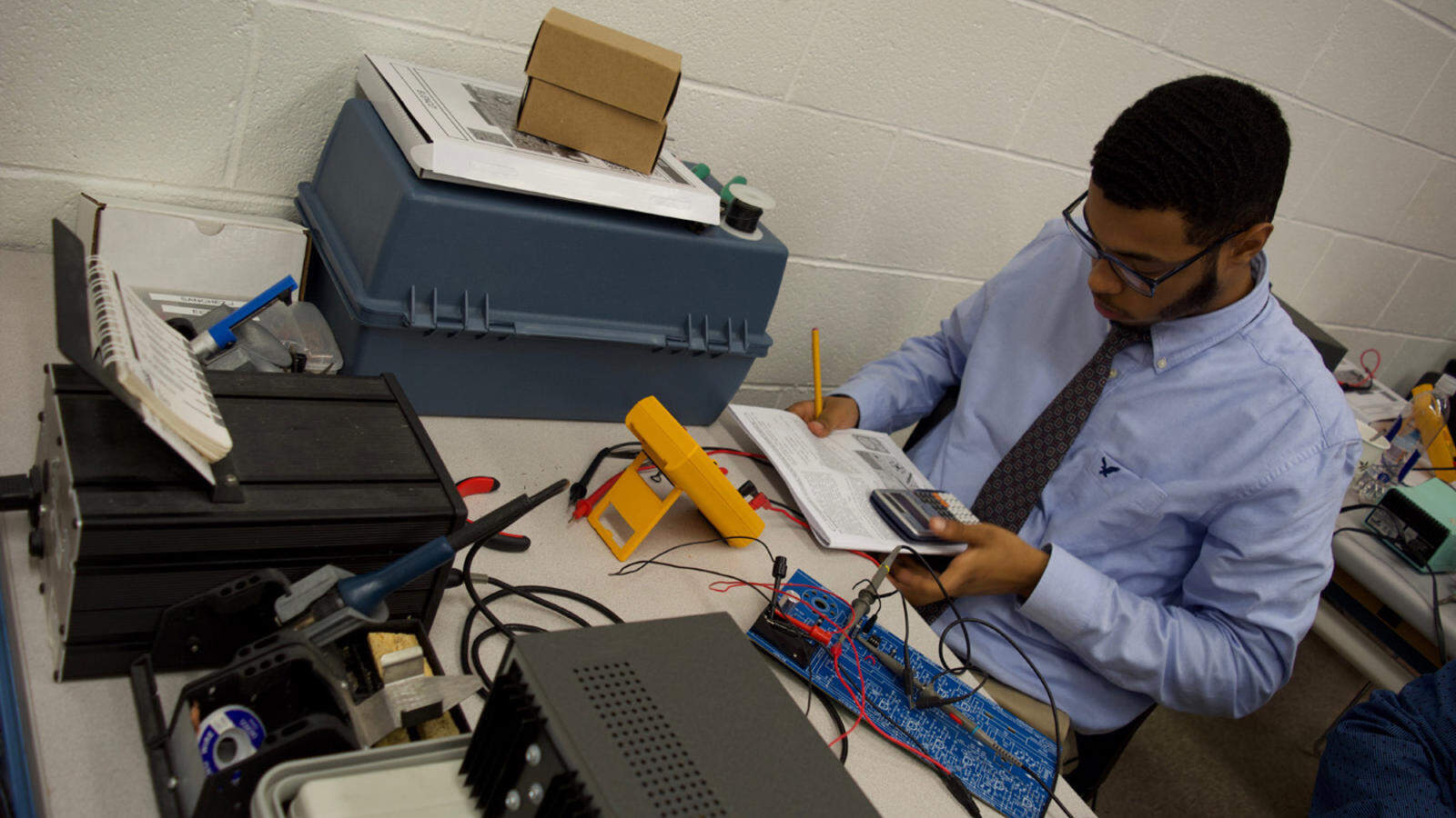 An electronics tech performs calculations using a calculator and readings from a multi-tester.