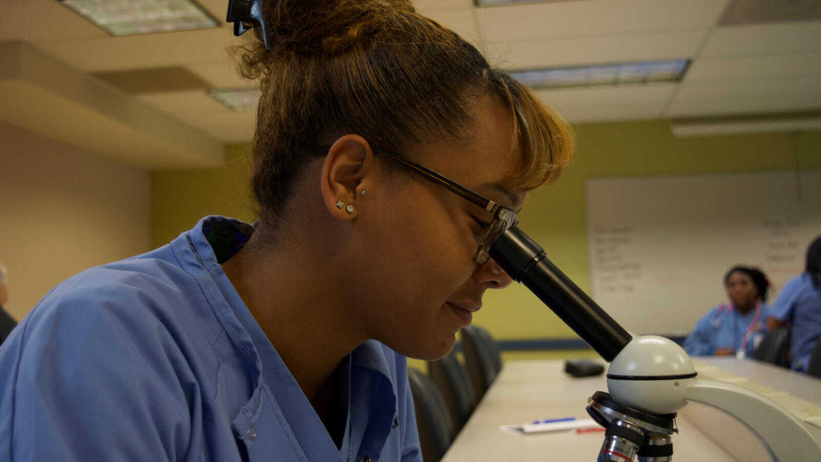 A student of the medical assistant program examines a specimen under a microscope