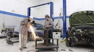 An auto body student works with a pneumatic cutter on a small steel structural piece - wide angle
